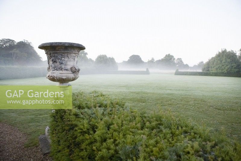 Old urn by Yew hedge. Distant mist in the early morning.