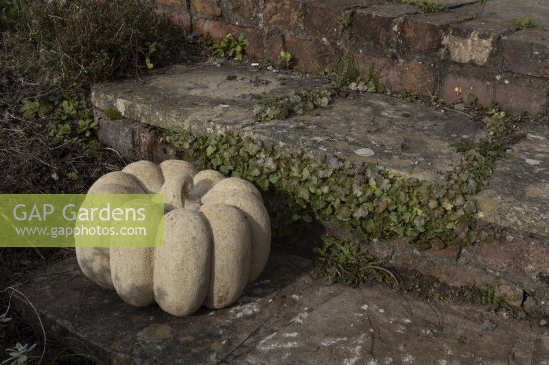 Pumpkin, a Bath stone sculpture, made by Zoe Singleton, set on the edge of a paved step. 