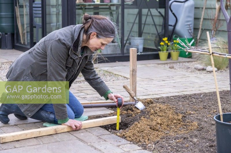 Woman measuring the depth of the hole for the wooden post to go in