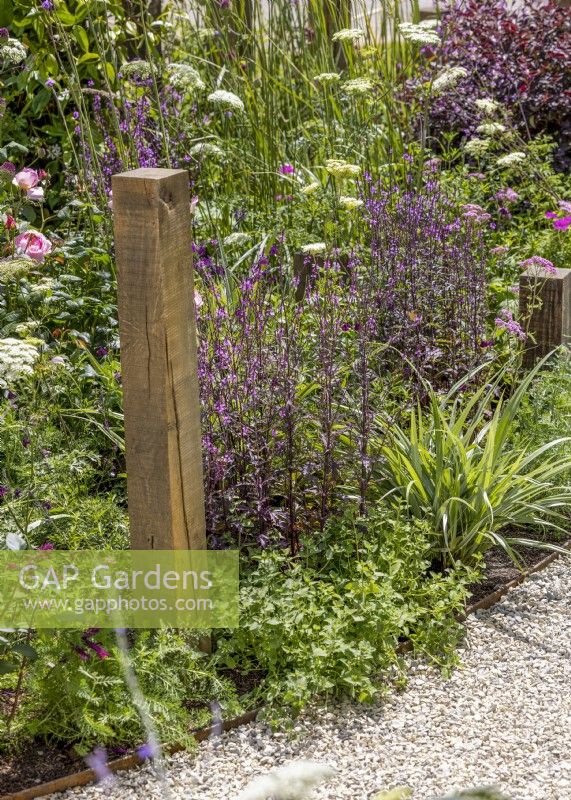 Caption Wooden post in a colourful perennial bed, summer June