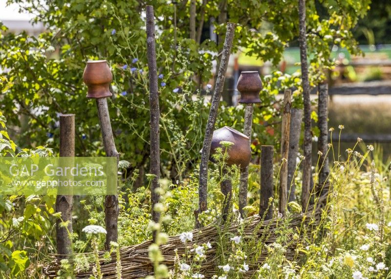 Woven hurdle fence topped with upturned pots, summer July