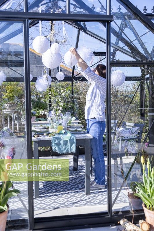 Woman hanging paper pom poms in greenhouse