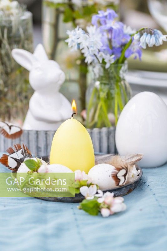 Egg shaped candle with smaller eggs, feathers, blossom and rabbit figure as easter decorations