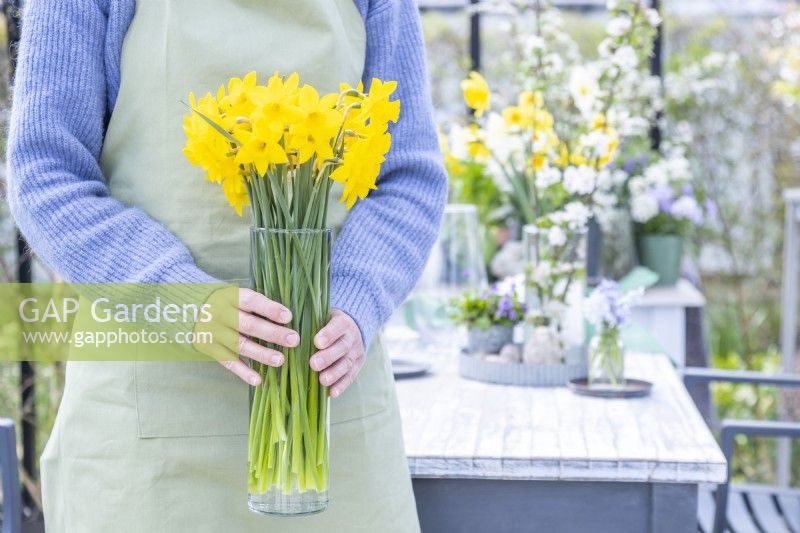 Woman holding a glass vase full of daffodils