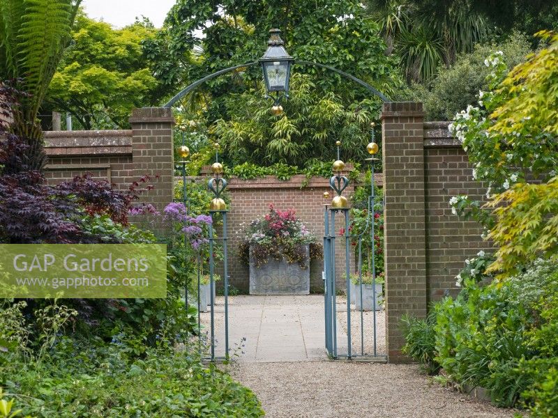 Entrance Court at East Ruston Old Vicarage Gardens, Norfolk, decorative iron work gateway, walls and containers at the beginning of Summer June