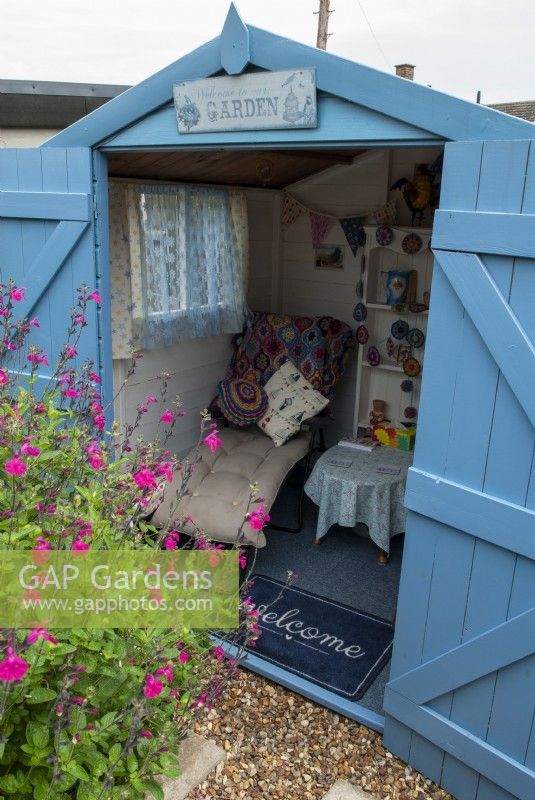Summerhouse converted from a garden shed, painted blue and simply furnished with pink Salvia microphylla bordering gravel path - Open Gardens Day, Copdock, Suffolk