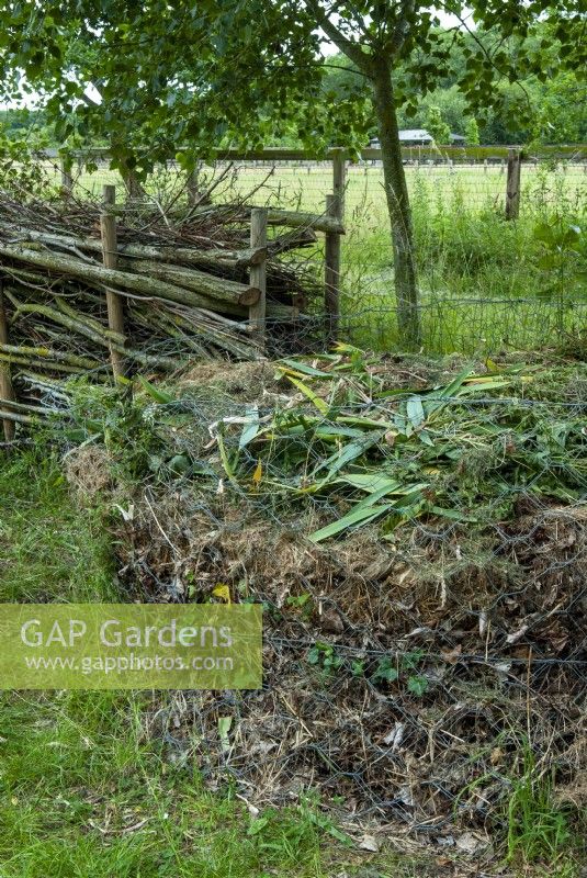 Circular compost heap within wire netting surround and dead boughs stacked between poles beyond - Open Gardens Day, Easton, Suffolk