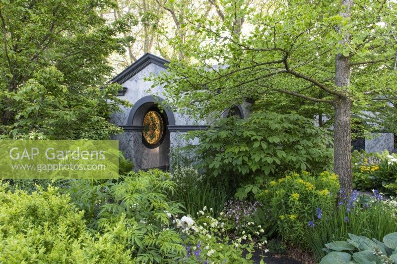 A tranquil woodland garden planted with specimen trees and shade-loving herbaceous plants surrounds a neo-classical temple. 