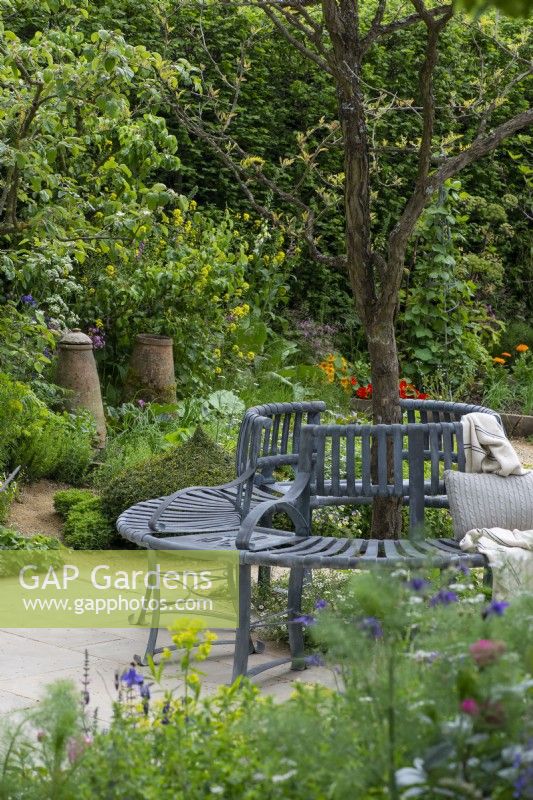 A metal tree seat is at the heart of a seasonal potager filled with ornamental and edible plants, combined in formal or informal schemes, in borders or raised beds.