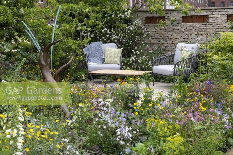 A secluded terrace surrounded by naturalistic borders of wildlife-friendly plants: Japanese snowball bush, foxgloves, ragged robin, hardy geranium and buttercups.