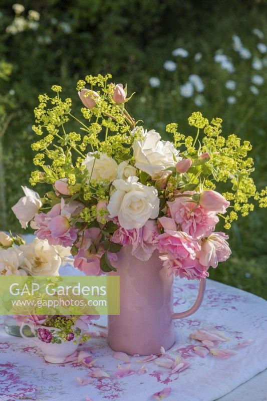 Pink and white roses with Alchemilla mollis displayed in a pink china jug on printed tablecloth
