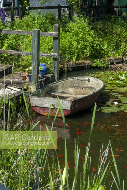 Boat on garden pond with rustic steps and handrail leading to it - Open Gardens Day, Shelfanger, Norfolk