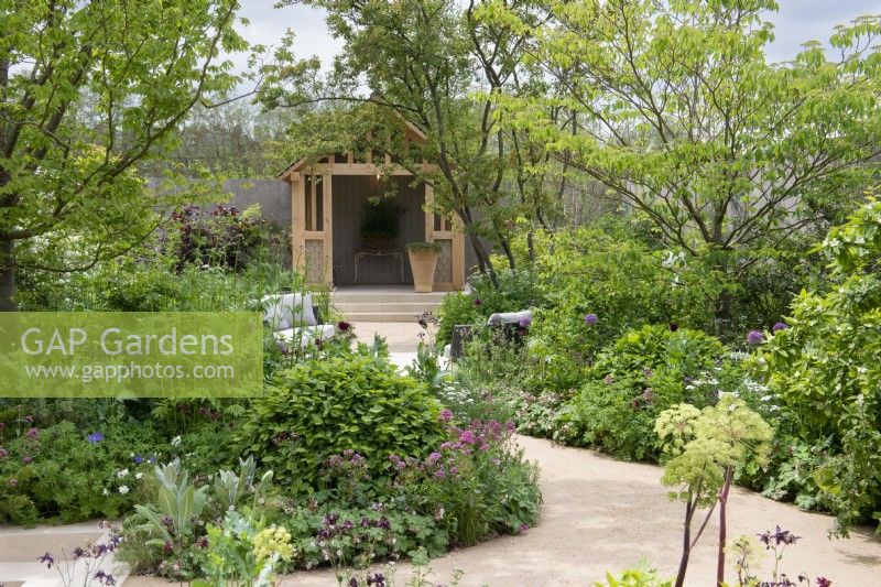 In a walled area, a summerhouse overlooks a seating area immersed amongst borders planted with a range of trees, shrubs and perennials to foster biodiversity.