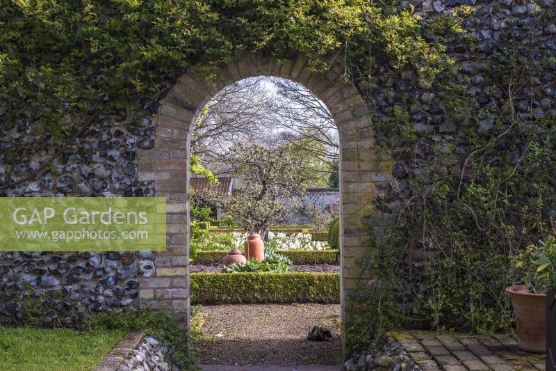 View through archway in flint wall into spring walled vegetable garden