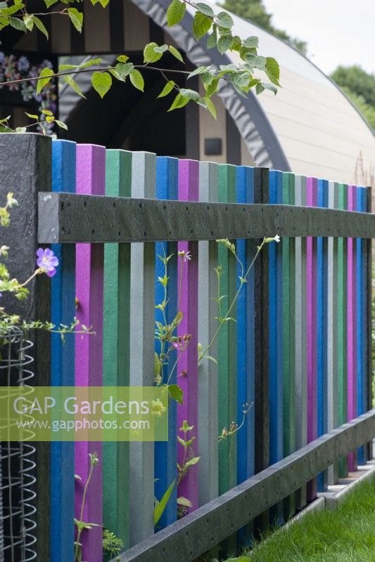 A picket fence built from reclaimed timber is painted in bright colours, a playful way of upcycling waste materials.