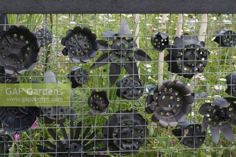 An imaginative way of upcycling waste plastic plants pots by scalloping the edges to create mock flowers, and fixing them to wire fencing.