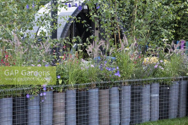 A low boundary is created from metal gabions filled with plastic plant pots, a clever way of upcycling waste plastic. The topmost pots are planted with grasses and flowering perennials.
