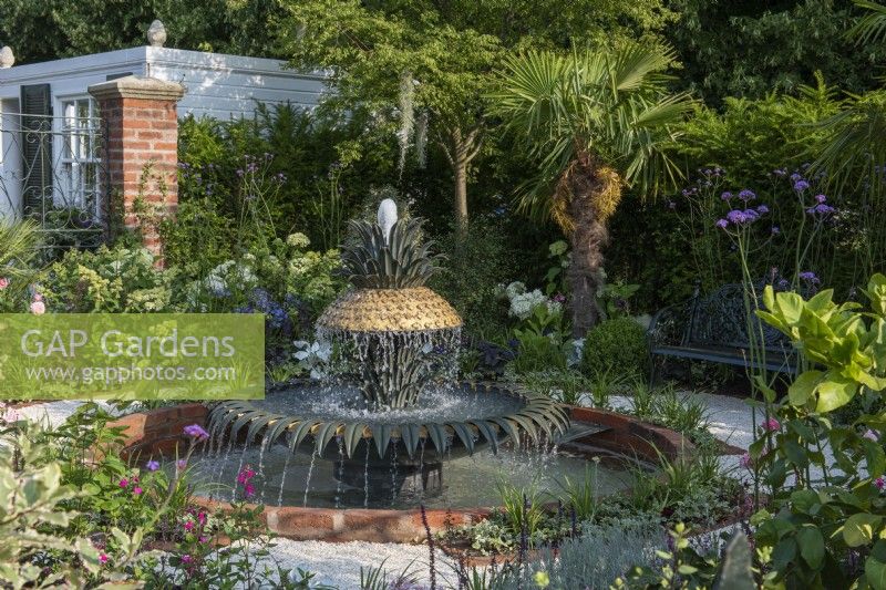 A formal courtyard garden inspired by Charleston, South Carolina, has a central pineapple shaped fountain, surrounded in beds of palms and exotics combined with shrub roses, hydrangeas and perennials. Paths are laid with crushed shells.