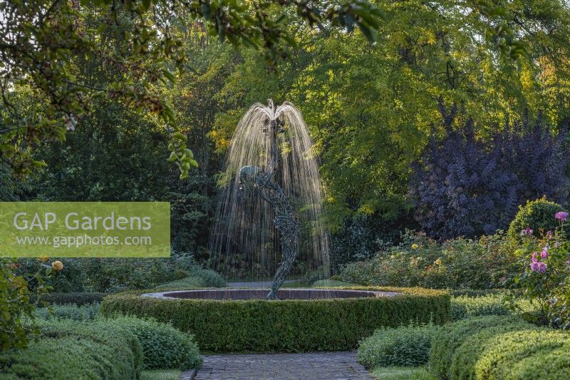 View of a contemporary figurative fountain as focal point in a formal country garden in late Summer - September