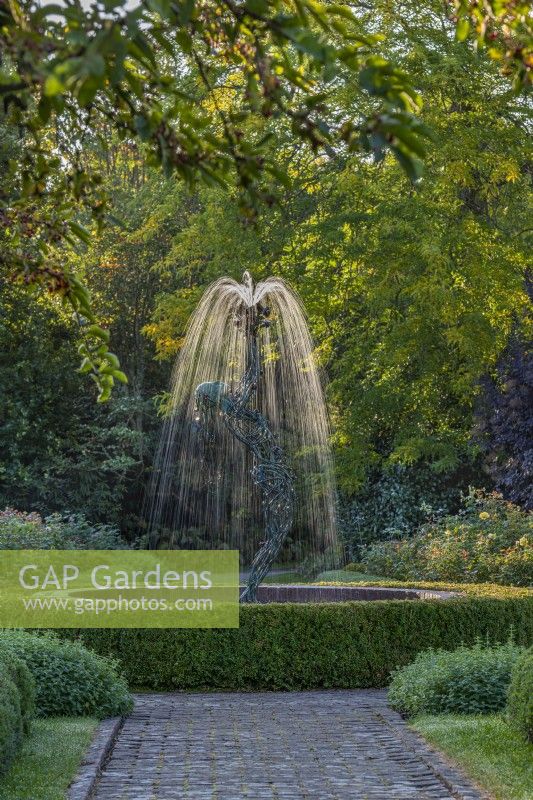 View of a contemporary figurative fountain as focal point in a formal country garden in late Summer - September