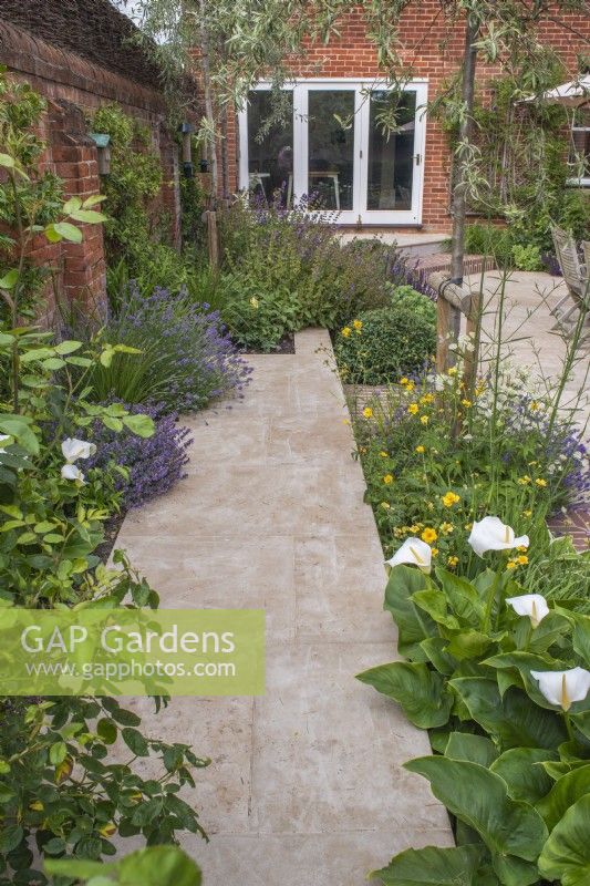 Sandstone paved path running along brick wall with borders in courtyard garden