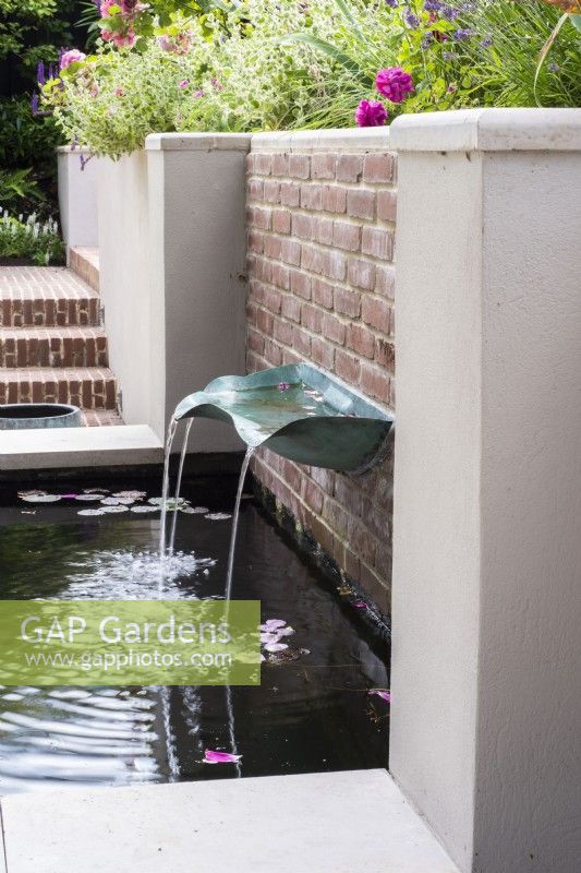 Verdigris metal basin fountain on brick wall of white rendered raised water feature