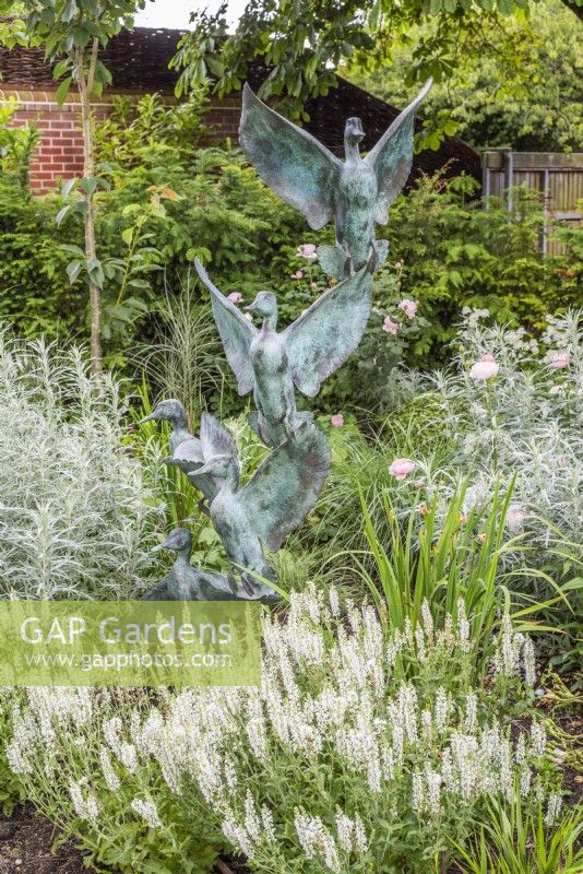 White border with wild duck metal verdigris sculpture .  Plants inc: Salvia sylvestris 'Schneehugel', Rosa 'Desdemona' and 'Queen of Sweden'; Artemisia 'Valerie Finnis' 