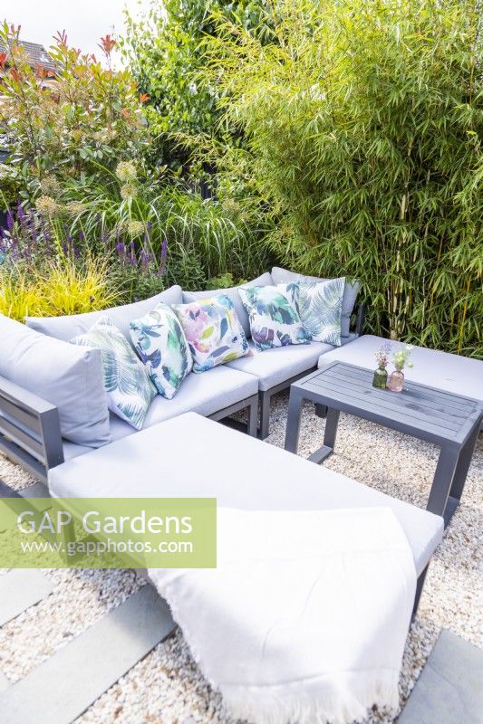 Sofa in gravel garden with cushions and blankets in front of raised bed and next to bamboo