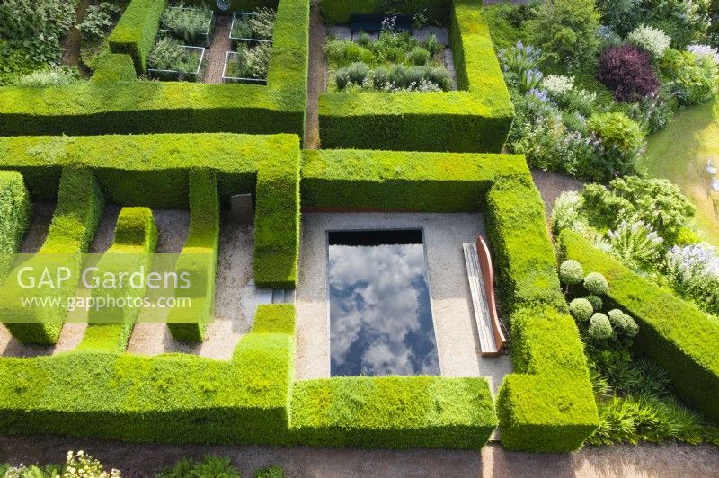 Clipped formal hedges of Taxus baccata - Yew, forming garden rooms, one containing a pool with dramatic reflections of the cloudy sky. Image taken with drone. June. Summer. 