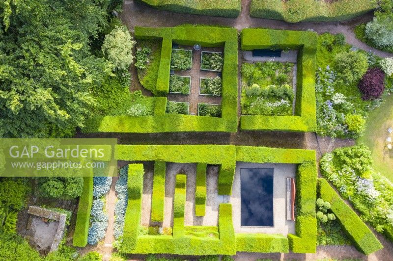 View over mature clipped hedges of Taxus baccata which form formal garden rooms of smaller gardens. June. Summer. Image taken with drone. 