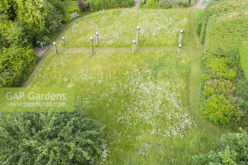 View over meadow with formal avenue of cut grass lined with wooden posts topped with stainless steel globes. June. Summer. Image taken with drone. 
