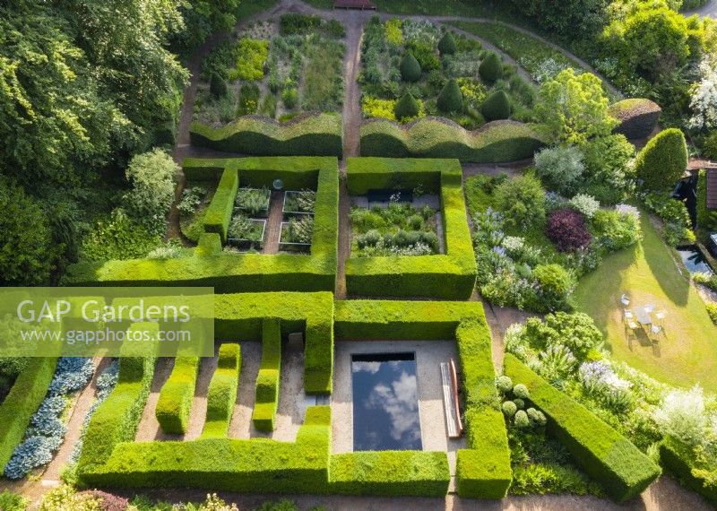 View over mature clipped hedges of Taxus baccata which form formal garden rooms of smaller gardens. Also a wave-form hedge of Beech with an area planted with ornamental grasses. June. Summer. Image taken with drone. 