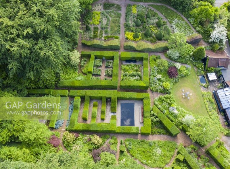 View over mature clipped hedges of Taxus baccata which form formal garden rooms of smaller gardens. Also a wave-form hedge of Beech with an area planted with ornamental grasses. June. Summer. Image taken with drone. 