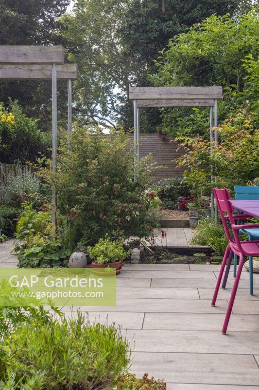  Small paved urban garden featuring recycled single pergolas with scaffold poles and half oak sleepers.