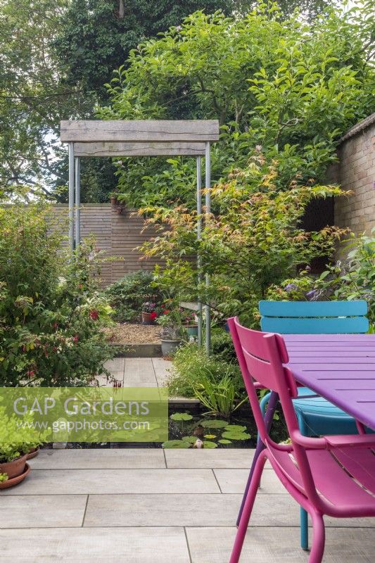 Single pergola constructed from scaffold poles and half oak sleepers in small enclosed urban garden with rectangular pool and seating
