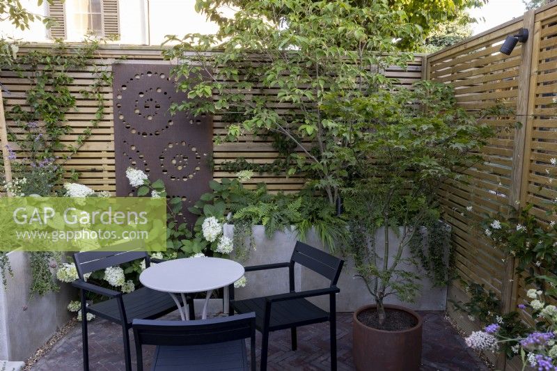 Courtyard garden with seating area with raised beds and contemporary wood boundary fence with metal screen