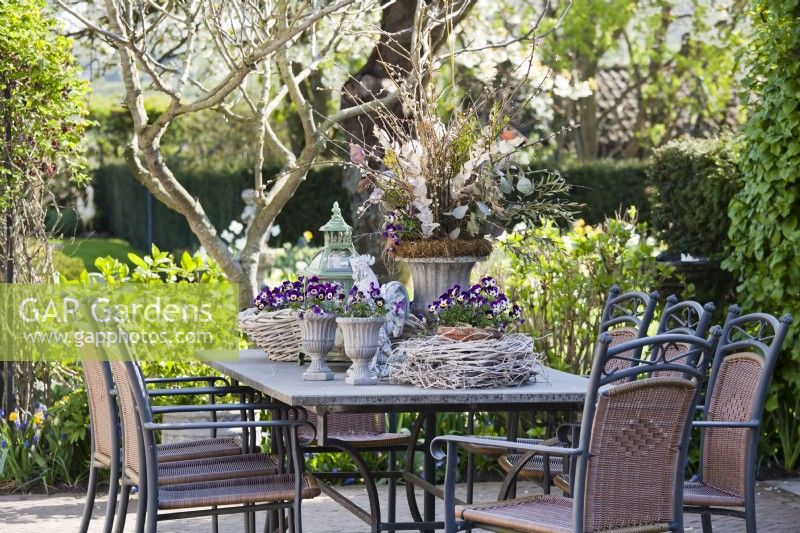 Outdoor table arrangement with decorative urns and a pot planted with Violas.