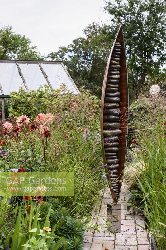 Seed Pod by Ted Edley surrounded by orange and purple planting including dahlias and grasses in September