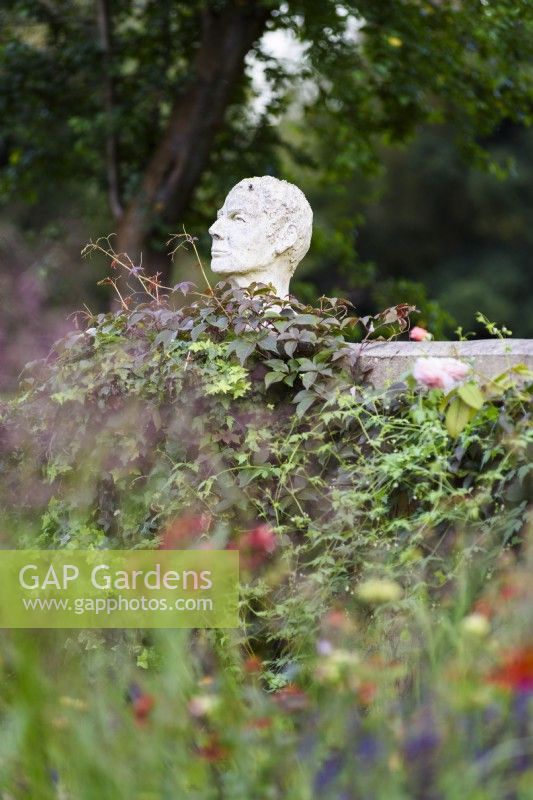 Sculpture of a man's head mounted on a wall in a country garden