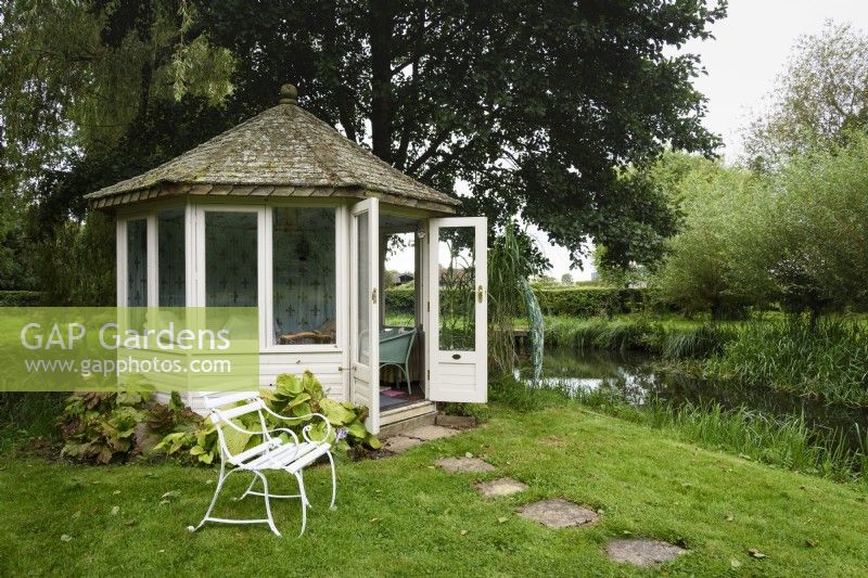 Summerhouse on an island in a large pond in a country garden in September