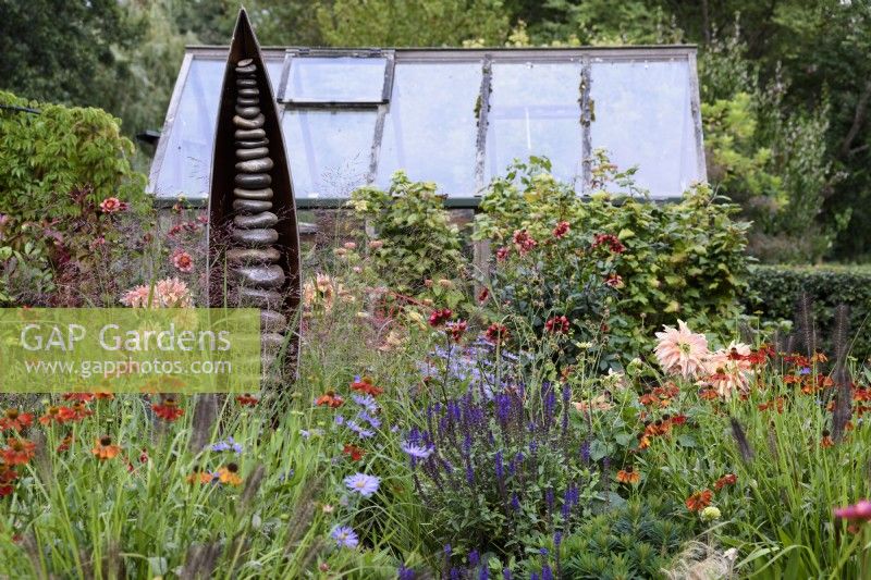 Colourful border of purple and orange including salvias, asters, heleniums and dahlias in front of Seed Pod by Ted Edley in September