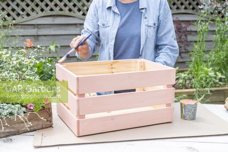 Woman painting wooden crate with pale orange pastel paint