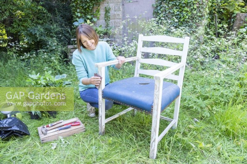 Woman using sandpaper to remove the last of the paint from the chair