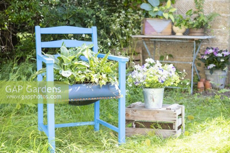 Chair container planted with Fatsia, Hostas and Ferns next to bouquet of flowers on a crate