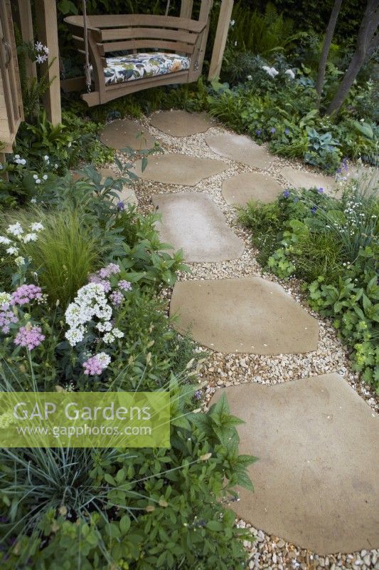 The London Square Community Garden. Design: James Smith Sanctuary Garden: RHS Chelsea Flower Show 2023. Natural stone and gravel pathway through borders to seating area. Summer.
