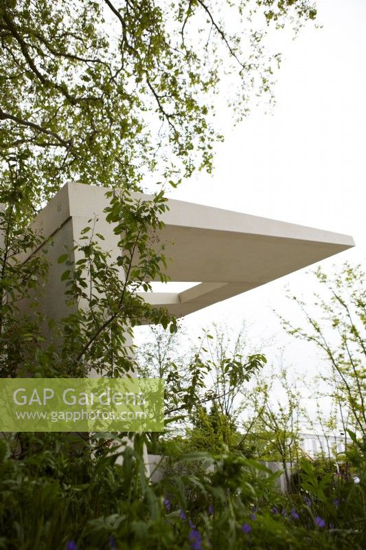 Memoria and GreenAcres Transcendence Garden. Designers: Gavin McWilliam and Andrew Wilson. Chelsea Flower Show 2023. Contemporary cantilevered pavilion against a stark white sky.