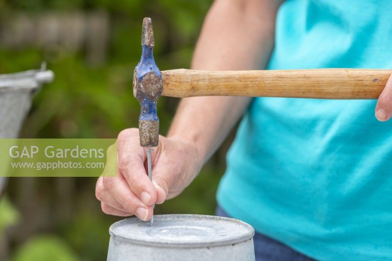 Woman using hammer and nail to make drainage holes in the bottom of the metal buckets