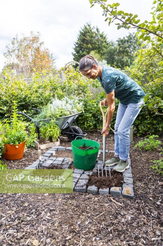 Woman mixing in compost with the soil in the open squares