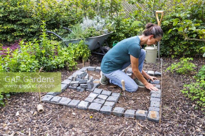 Woman placing Granite setts in a checkerboard pattern with a square outline