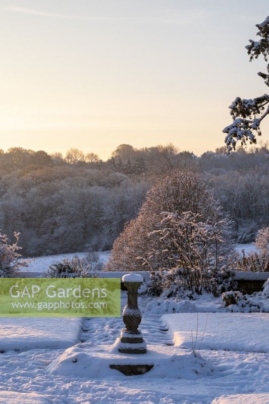 The garden at Gravetye Manor, Sussex, in winter. A view across the garden with a sundial, beneath heavy snow